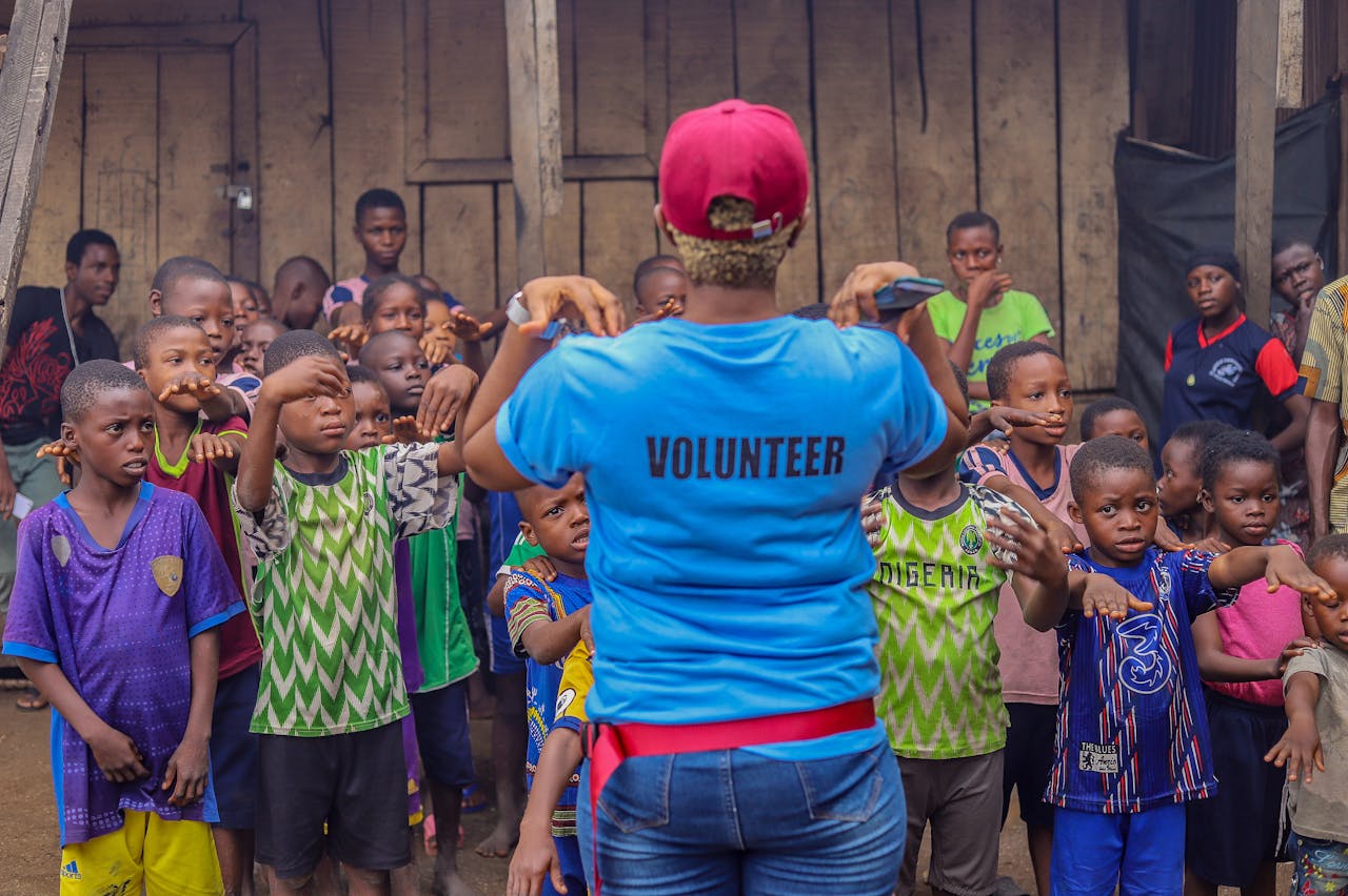 A volunteer guides a diverse group of children in an outdoor activity, fostering community spirit and teamwork.